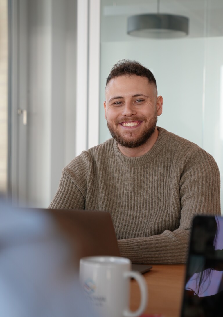Lachender Mann sitzt an einem Schreibtisch.