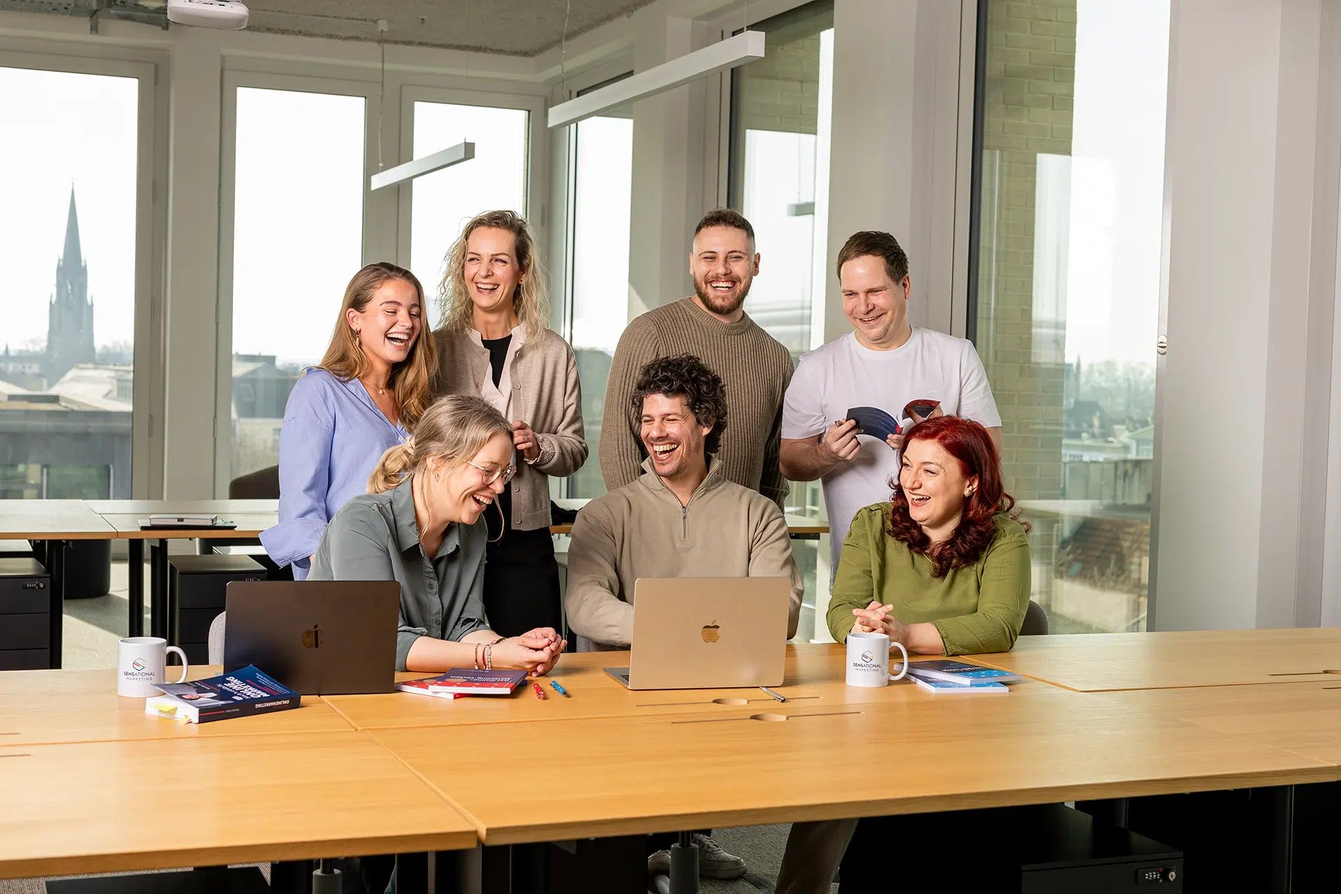 Ein Team in einem großen Büro lacht an einem langen Tisch